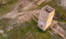 Se ve una torre de piedra vista desde arriba con un prado verde y marrón alrededor de la misma