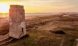 Imagen del atardecer con la torre de castilnovo a media distancia y el color rosado sobre el mar al fondo